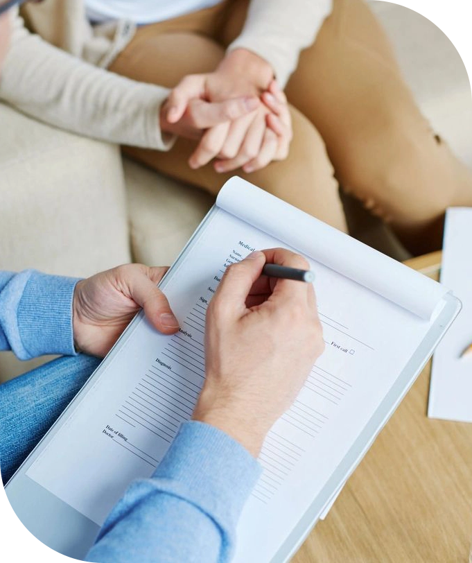 A person writing on paper with another person sitting next to it.